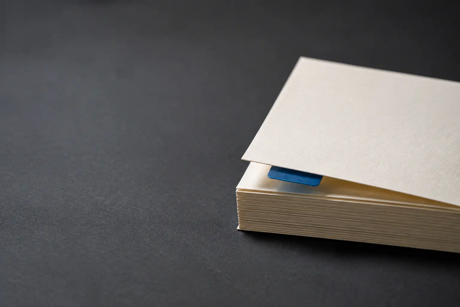 Real compact stack of blank ivory cards with exactly one cobalt tab raising the top card